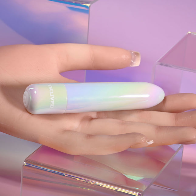 Hand holding an Evolved EASY DOES IT Pearlescent White Lipstick Vibrator against a soft, multicolored background