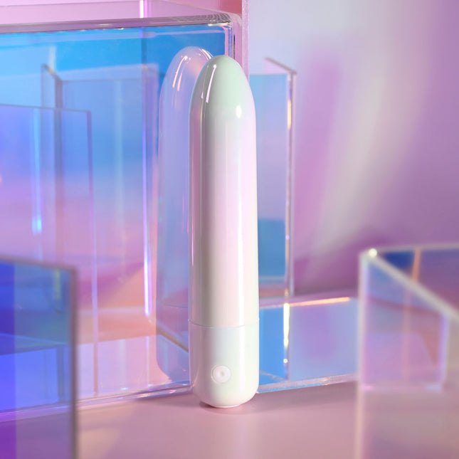 Evolved EASY DOES IT Pearlescent White Lipstick Vibrator with a pink base on a reflective surface with a pastel gradient background