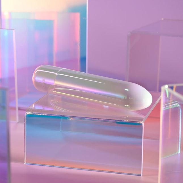 Evolved EASY DOES IT Pearlescent White Lipstick Vibrator cylindrical object on a clear stand with a pastel gradient background