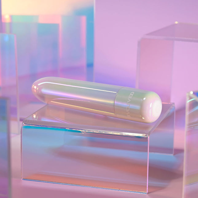 Neon cylindrical Evolved EASY DOES IT Pearlescent White Lipstick Vibrator on a transparent platform with a pastel gradient background