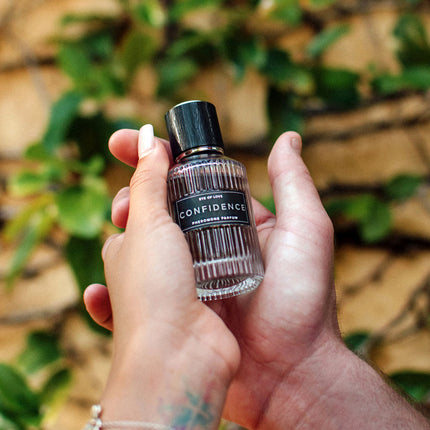 Hand holding a small bottle labeled 'Confidence' against a natural background