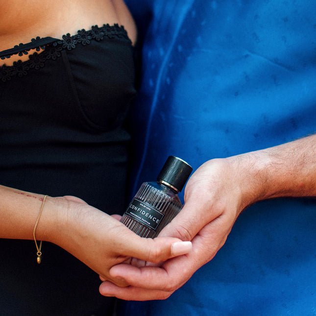 Person holding a perfume bottle labeled 'Confidence' against a blue background