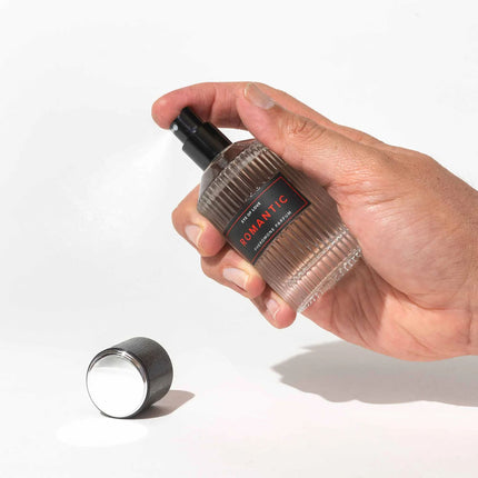 Hand holding a transparent bottle with a black cap labeled 'Romantic' on a white background