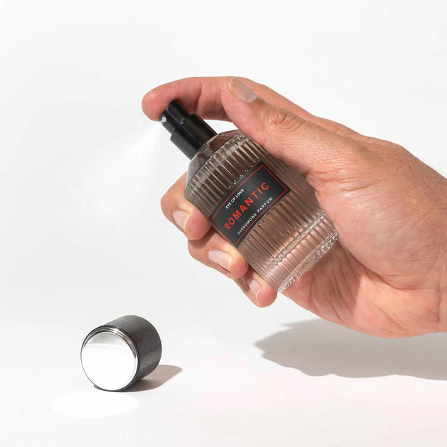 Hand holding a transparent bottle with a black cap labeled 'Romantic' on a white background
