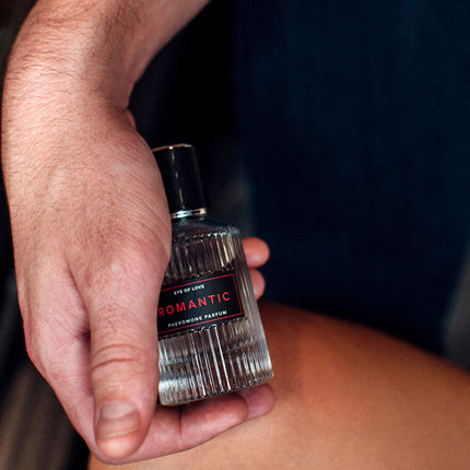 Hand holding a small perfume bottle labeled 'Romantic' against a dark background
