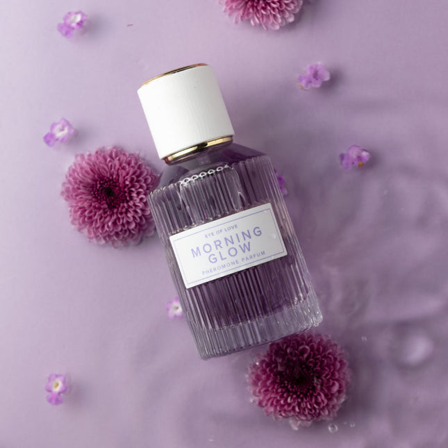 Perfume bottle labeled 'Morning Glow' surrounded by purple flowers on a light purple background