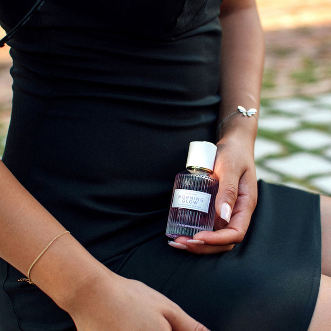 Person holding a small bottle labeled 'Morning Glow' outdoors.
