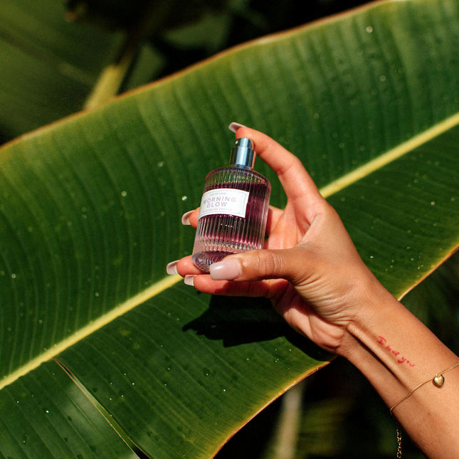 Hand holding a small bottle of perfume against a green leaf background