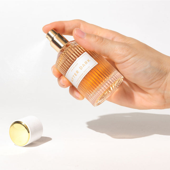 Hand holding a after dark perfume bottle with a white label on a light background