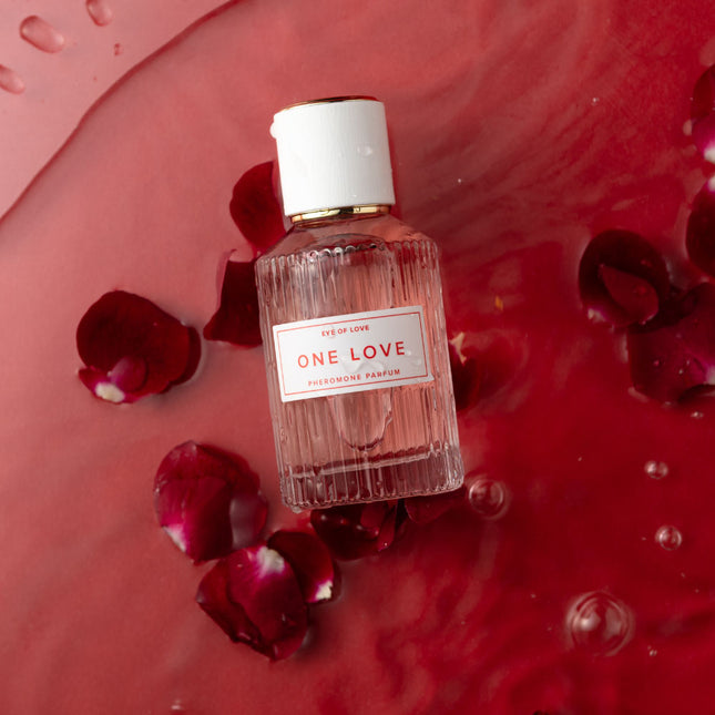 Perfume bottle labeled 'One Love' surrounded by red rose petals on a red background