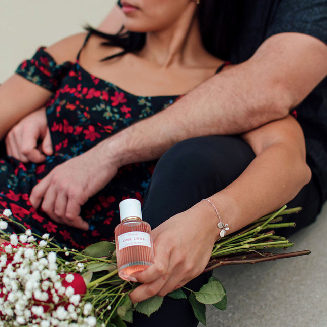 Person holding a bottle of perfume with flowers on a neutral background