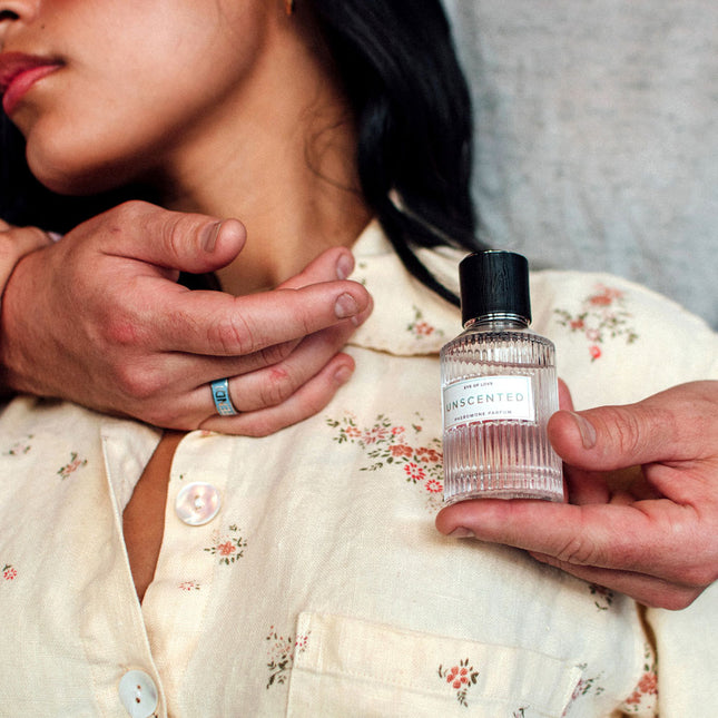 Person holding a bottle of Eye Of Love Unscented Pheromone Perfume - 50ml near another person's neck.