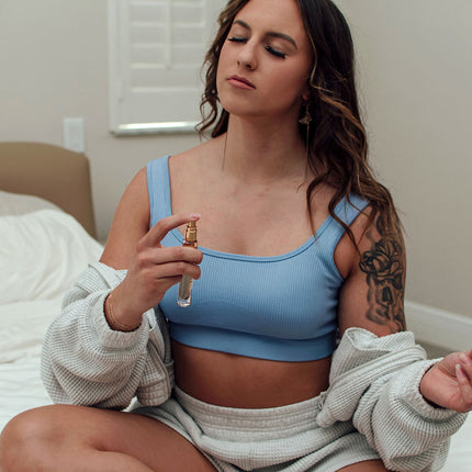 Woman in a blue sports bra holding a pheromone perfume bottle indoors.