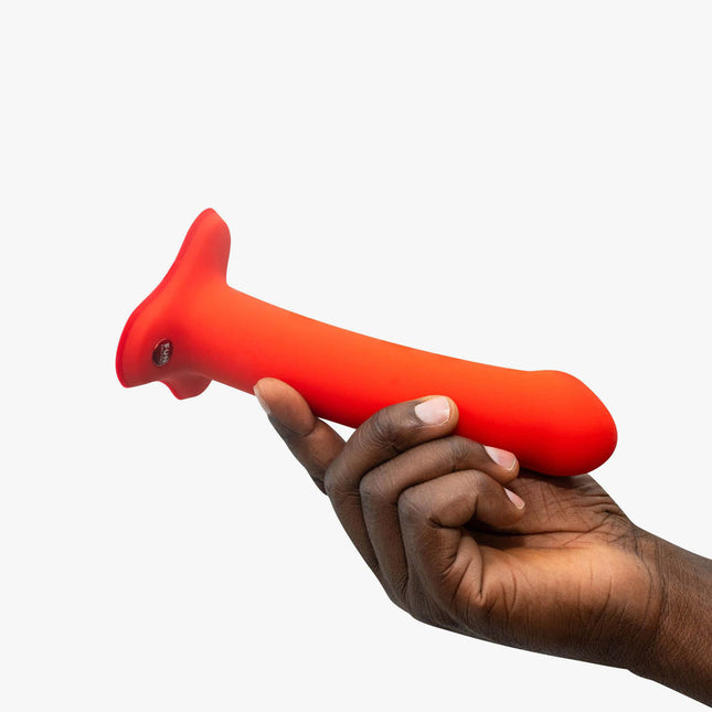 hand holding a FUN FACTORY MAGNUM Orange – Strap-On 7 Inch Dildo, Hands-Free on a white background
